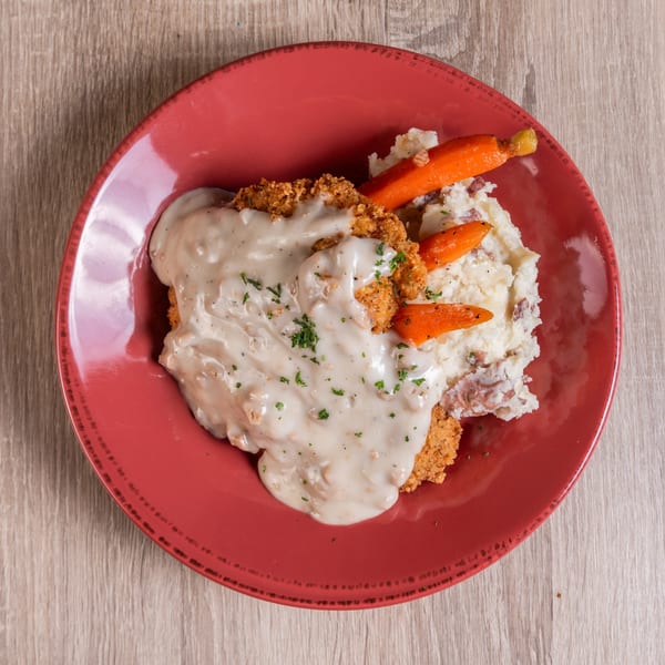 Chicken fried steak with gravy, mashed potatoes, and roasted carrots on a red plate.