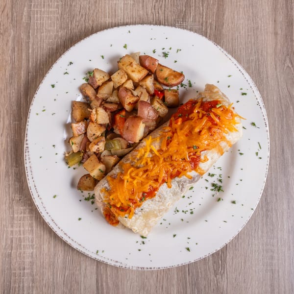 Breakfast burrito topped with red sauce and shredded cheese, served with roasted potatoes.