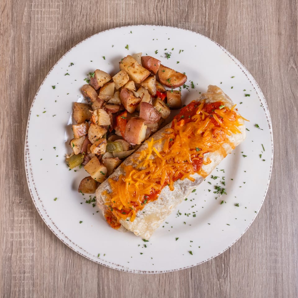 Breakfast burrito topped with red sauce and shredded cheese, served with roasted potatoes.