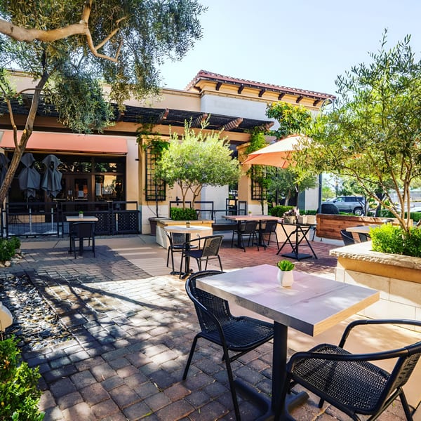 RANGE kitchen & tap's outdoor patio with tables, chairs, umbrellas, and lush greenery under sunny skies.