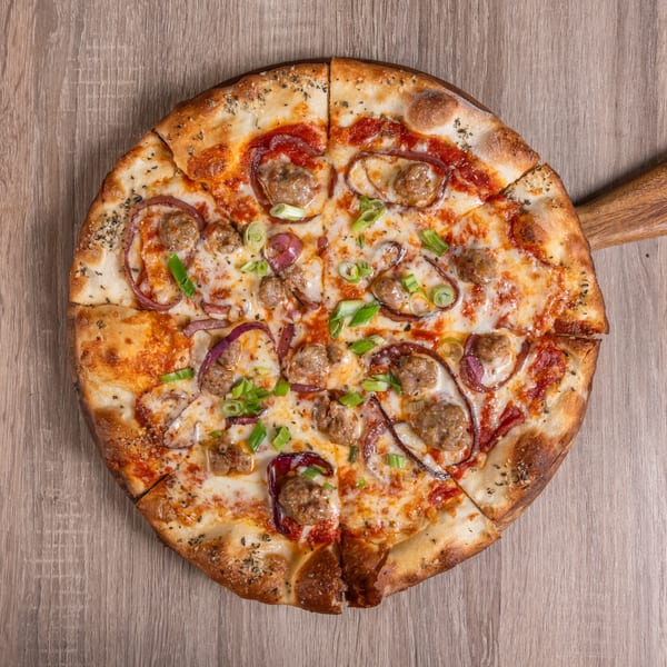 A whole RANGE kitchen & tap pizza with sausage, red onion, and green onions on a wooden board.