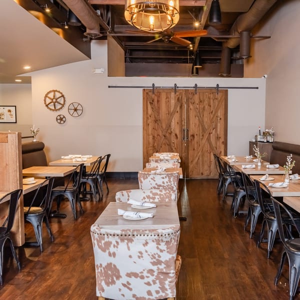 Dining room at RANGE kitchen & tap with wooden tables, black chairs, and cowhide upholstered seating.