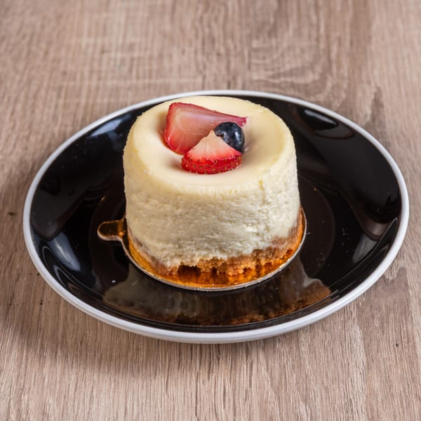 Mini cheesecake with a graham cracker crust, topped with fresh strawberries and blueberries on a black plate.