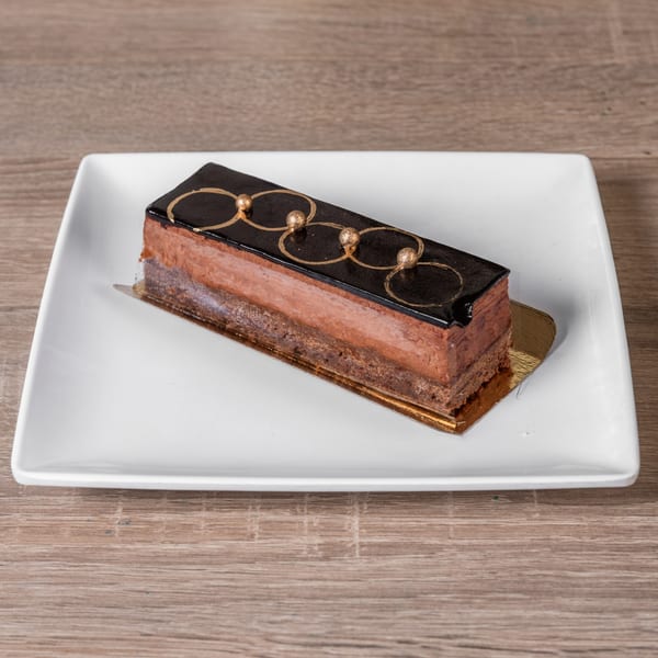 Rich chocolate cake with gold decorations on a white rectangular plate at RANGE kitchen & tap.