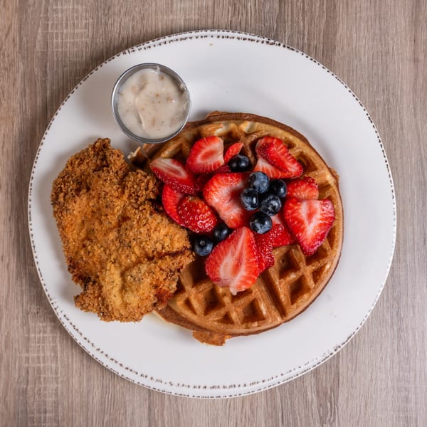 Crispy fried chicken and a waffle topped with fresh strawberries and blueberries, with a side of gravy.