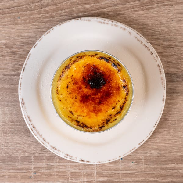 A crème brûlée with a caramelized sugar topping, served on a white plate on a wooden table.