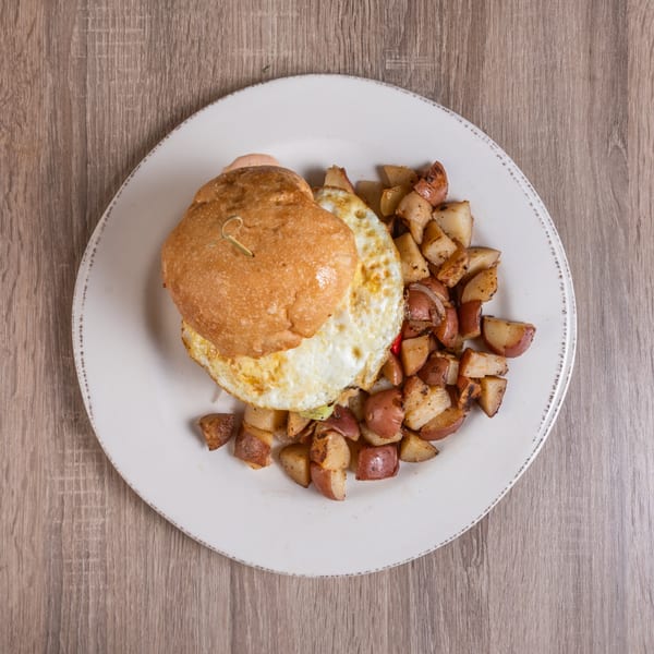 Breakfast sandwich with fried egg and bun, served with a side of roasted potatoes.